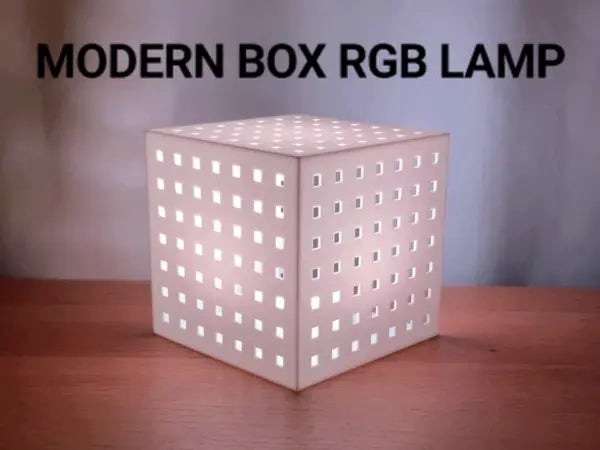 A 3D-printed cube-shaped modern RGB ambient lamp glowing on a desk, built around a remote-controlled RGBW LED puck